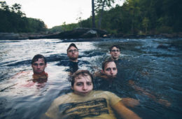Members of Of the Vine sitting in a river.