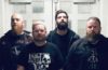 four dudes with beards and black tee shirts standing against steel doors