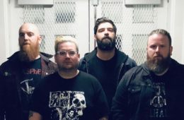 four dudes with beards and black tee shirts standing against steel doors