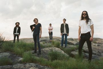 Members of Phantom Electric standing on a hill with storm clouds above.