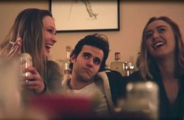 man sitting on couch next to two women drinking and smoking