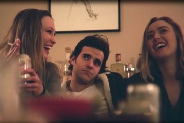 man sitting on couch next to two women drinking and smoking