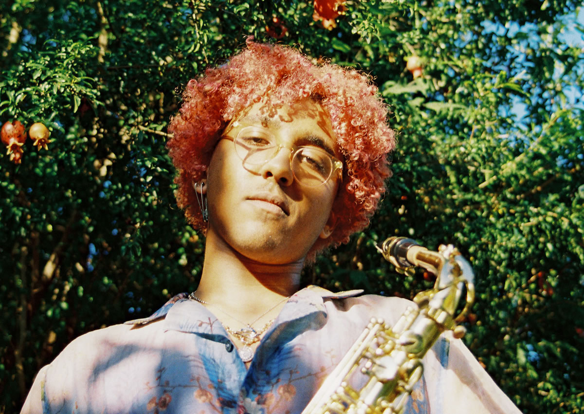 Atlanta artist Hio holding a saxophone in front of a tree