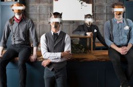 Members of Quiet Hounds wearing blindfolds and masks standing in front of a desk