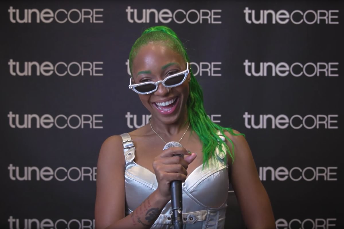 woman with green hair smiling with a microphone in TuneCore booth