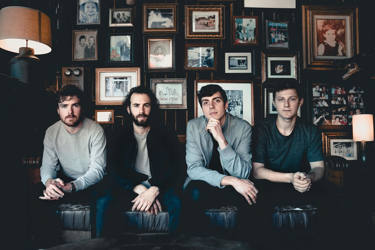 Members of Walden sitting on a couch with a wall of framed photos behind them