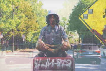 Akete sitting cross-legged next to a street sign.