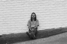 Zac Crook sitting against a white brick wall.