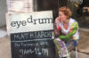 woman sitting and biting into apple next to an eyedrum sign