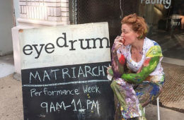 woman sitting and biting into apple next to an eyedrum sign