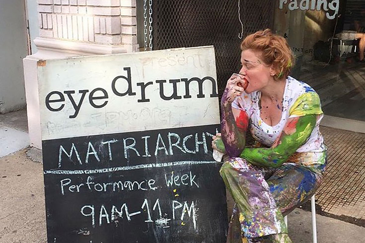 woman sitting and biting into apple next to an eyedrum sign