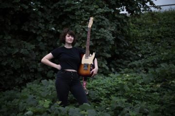 Gabbie Rotts standing in an ivy field holding an electric guitar
