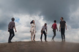 members of Karaoke standing on a hill with dark clouds behind them