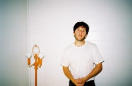 Drew Besking wearing a white t-shirt standing next to a gold lamp post