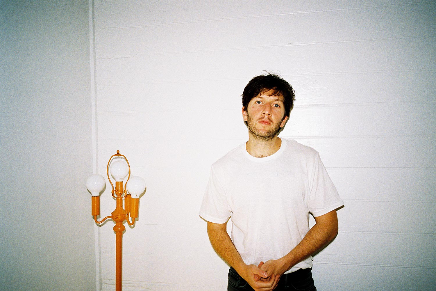 Drew Besking wearing a white t-shirt standing next to a gold lamp post