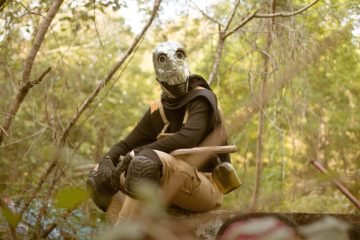 Man in a shiny disco ball mask crouching on the ground
