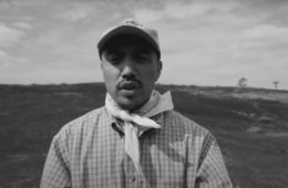 Victor Mariachi standing in a field wearing a baseball cap and scarf