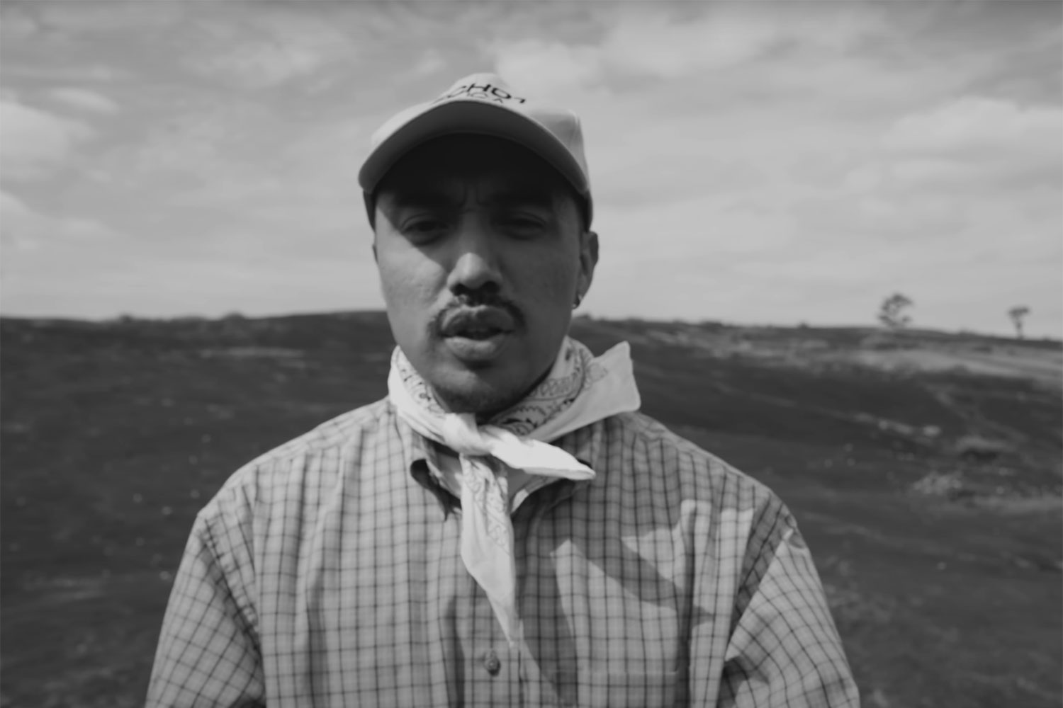 Victor Mariachi standing in a field wearing a baseball cap and scarf