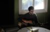 Alex Lotito playing an acoustic guitar and writing lyrics at a kitchen table