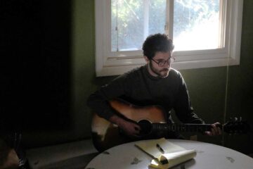 Alex Lotito playing an acoustic guitar and writing lyrics at a kitchen table