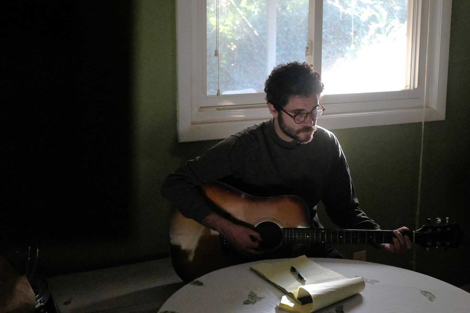 Alex Lotito playing an acoustic guitar and writing lyrics at a kitchen table